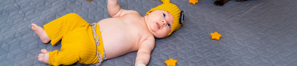 Bebê deitado sobre um tapete usando roupa amarela durante momento de descanso e desenvolvimento na primeira infância