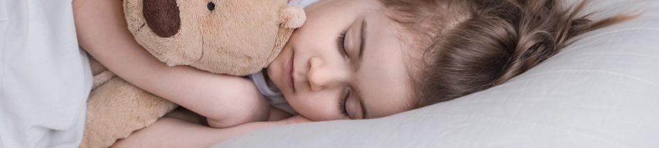 Criança dormindo tranquilamente na cama abraçada a um urso de pelúcia, representando o sono infantil saudável.